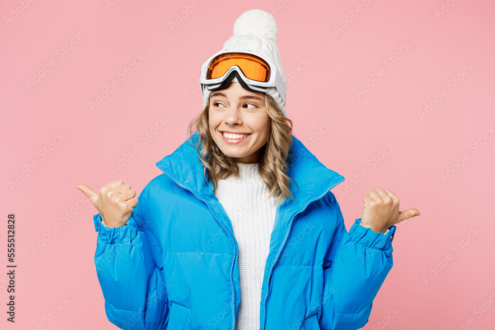 Snowboarder fun woman wear blue suit goggles mask hat ski padded jacket point thumb finger aside on area isolated on plain pastel pink background Winter extreme sport hobby weekend trip relax concept Snowboarder fun woman wear blue suit goggles mask hat ski padded jacket point thumb finger aside on area isolated on plain pastel pink background Winter extreme sport hobby weekend trip relax concept