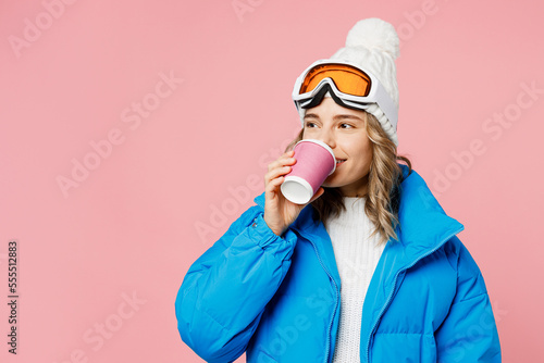 Snowboarder woman in blue suit goggles mask hat ski padded jacket hold cup coffee to go look aside area isolated on plain pastel pink background Winter extreme sport hobby weekend trip relax concept