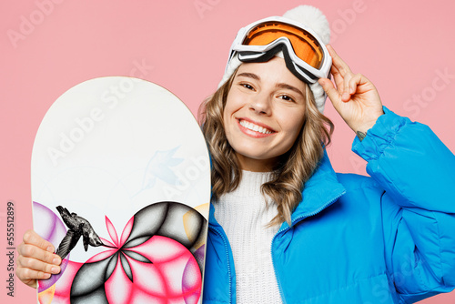 Close up snowboarder happy woman wear blue suit goggles mask hat ski padded jacket touch glasses wink isolated on plain pastel pink background. Winter extreme sport hobby weekend trip relax concept.