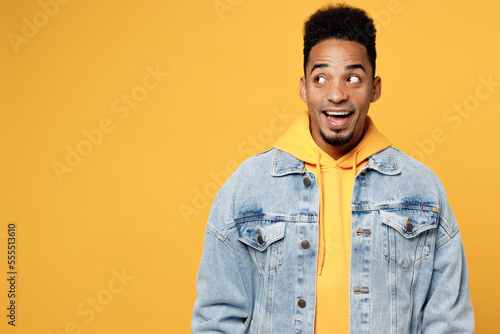 Young surprised shocked impressed man of African American ethnicity wear denim jacket hoody look aside on workspace area isolated on plain yellow background studio portrait. People lifestyle concept.