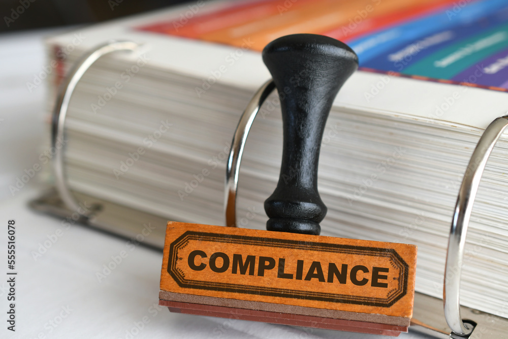 Compliance rubber stamp by binder of rules guidelines, changing procedures to adhere to regulations Compliance rubber stamp by binder of rules guidelines, changing procedures to adhere to regulations