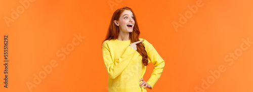 Look at that, wow. Impressed and fascinated, astonished cute redhead woman stare and pointing left with excited, happy smile, shoppaholic adore winter holiday sales, express interest and admiration