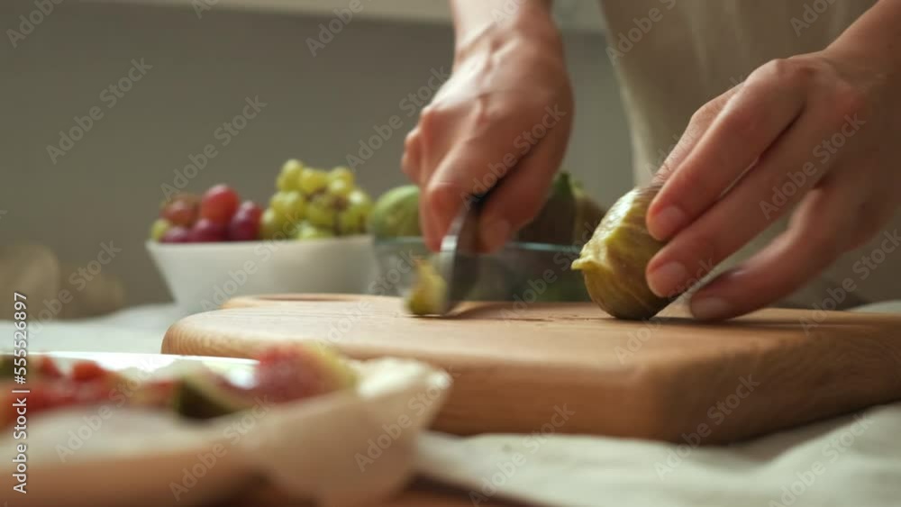 fresh cut figs close up. View of cutting fig fruit with knife. the girl cuts figs. women's hand cut ripe figs with a knife on a wooden board. women's hands spread sliced figs on a plate fresh cut figs close up. View of cutting fig fruit with knife. the girl cuts figs. women's hand cut ripe figs with a knife on a wooden board. women's hands spread sliced figs on a plate