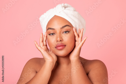 Attractive black body positive woman with smooth skin touching face and looking at camera, enjoying self-care routine