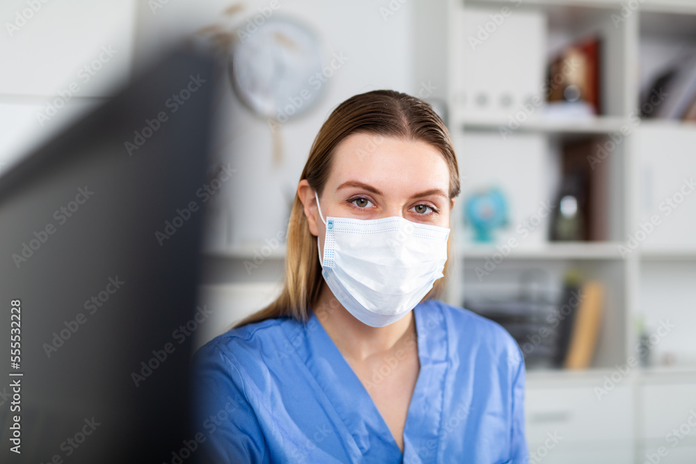 Female doctor in in protective medical mask working on laptop in clinic