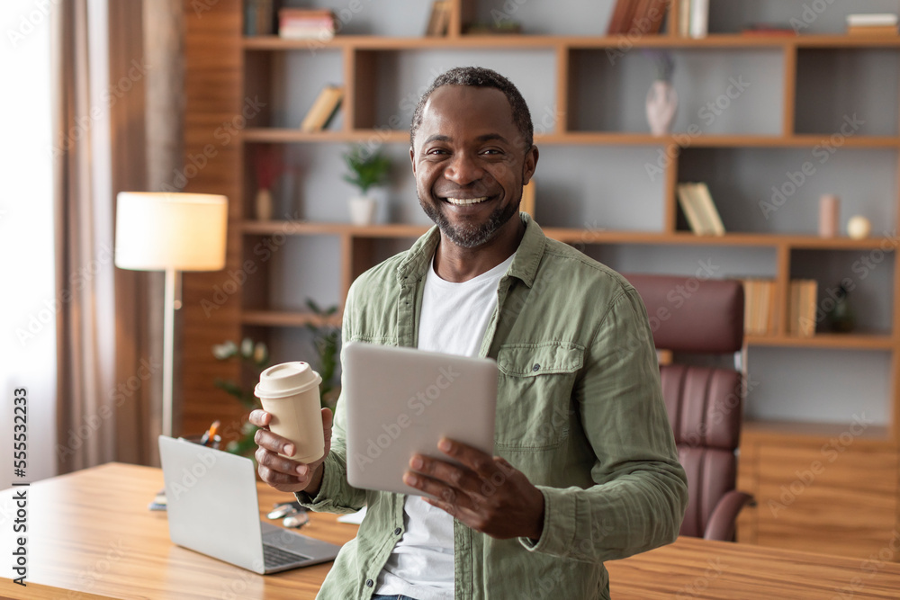 Cheerful handsome mature black businessman with tablet and cup of drink takeaway watch at camera Cheerful handsome mature black businessman with tablet and cup of drink takeaway watch at camera