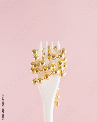 Christmas gold ornaments used on white fork as spaghetti against pastel pink background. Minimal style design.