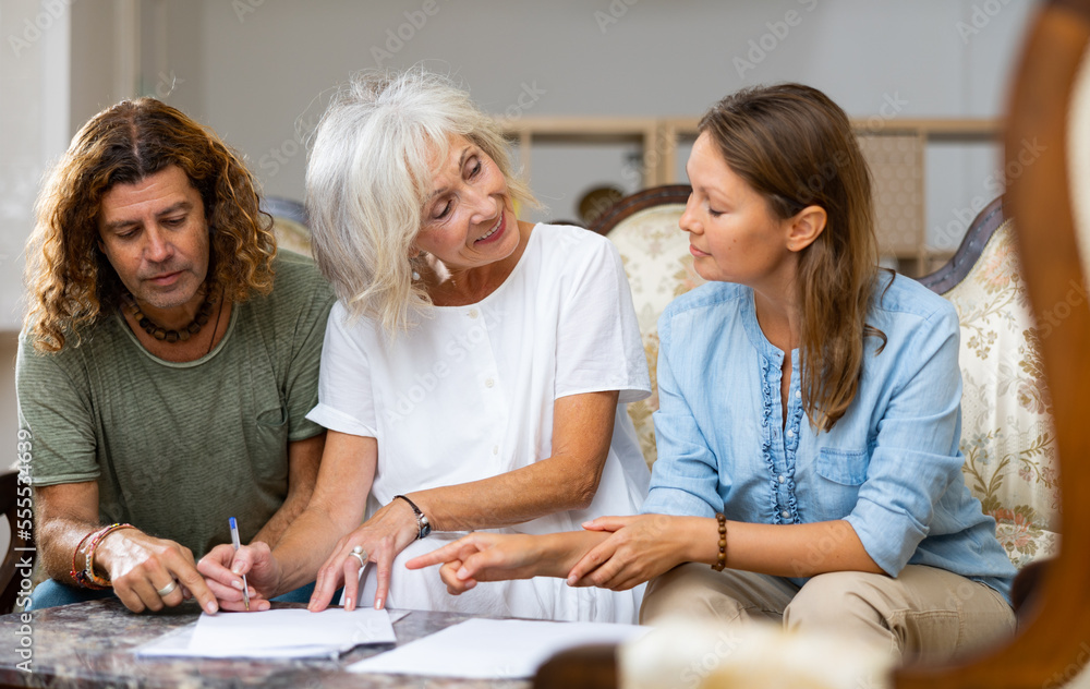 Fototapeta premium Mature mother and adult children fill out paperwork in home room