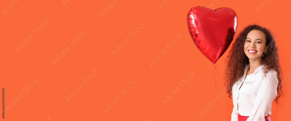 Pretty African-American woman holding heart-shaped balloon on orange background with space for text. Valentine's Day celebration Pretty African-American woman holding heart-shaped balloon on orange background with space for text. Valentine's Day celebration