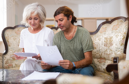 Aged woman and man sign documents sitting in luxury room interior