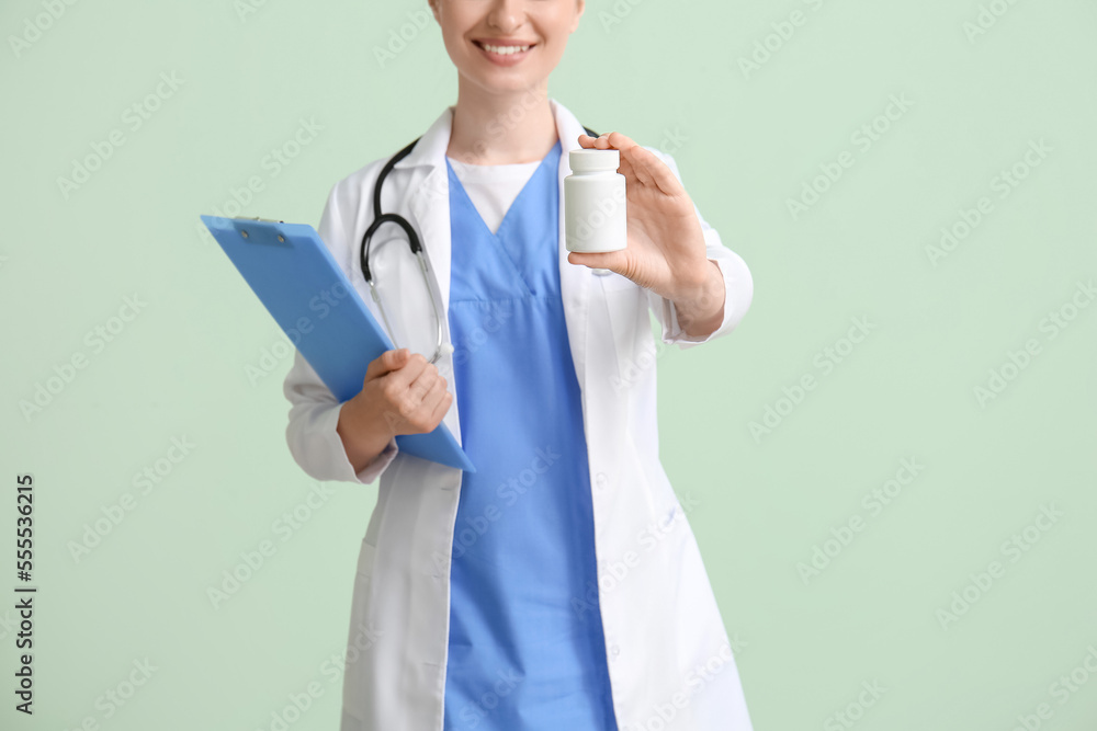 Female doctor with clipboard and bottle of vitamin A on green background Female doctor with clipboard and bottle of vitamin A on green background