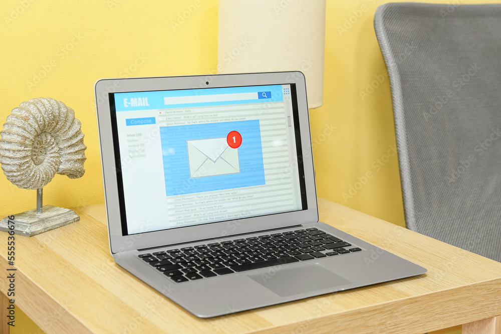 Fototapeta premium Modern laptop with opened e-mail box and decor on wooden table near color wall