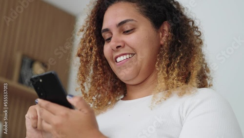 Happy black woman holding cell phone using smartphone device at home. Smiling young latin woman blogger subscribing new social media, buying in internet, ordering products online in apps.
 photo