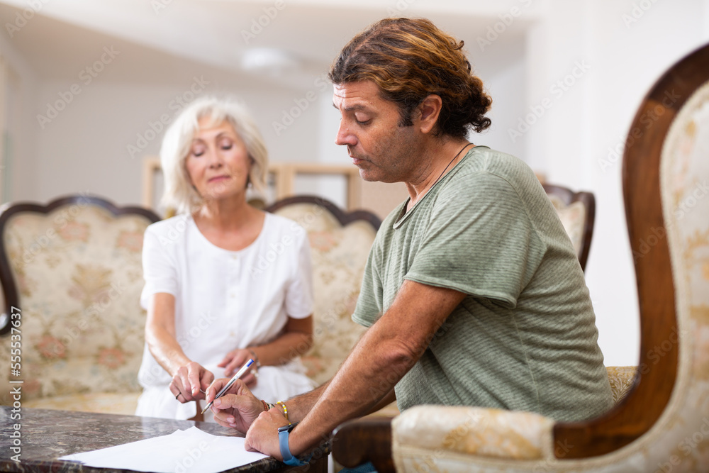 Obraz premium Middle aged man signing documents under close attention of aged woman