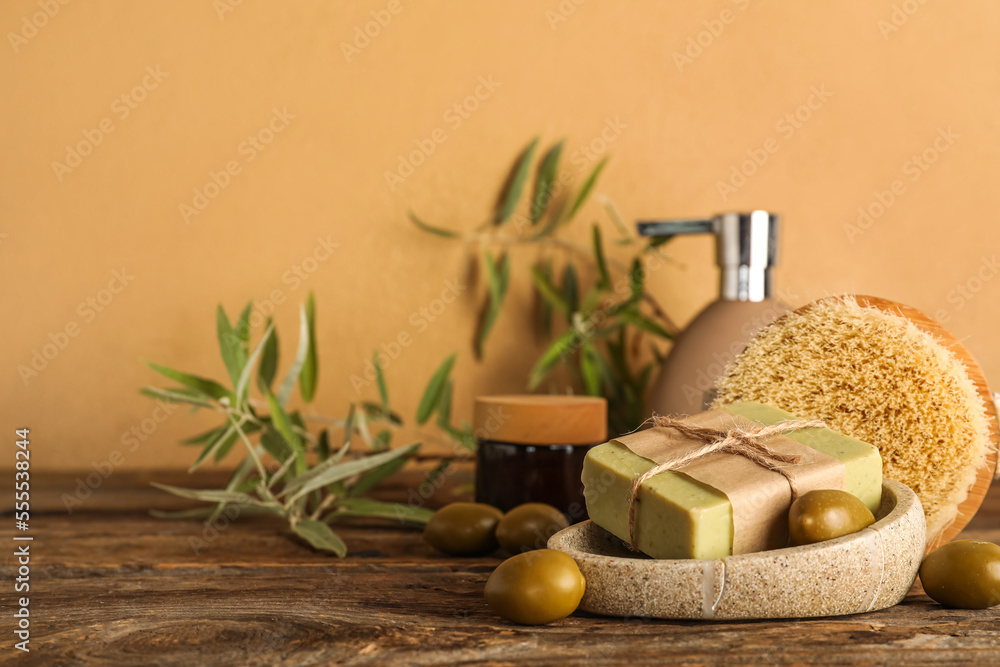 Holder with soap bar and green olives on table near beige wall, closeup
