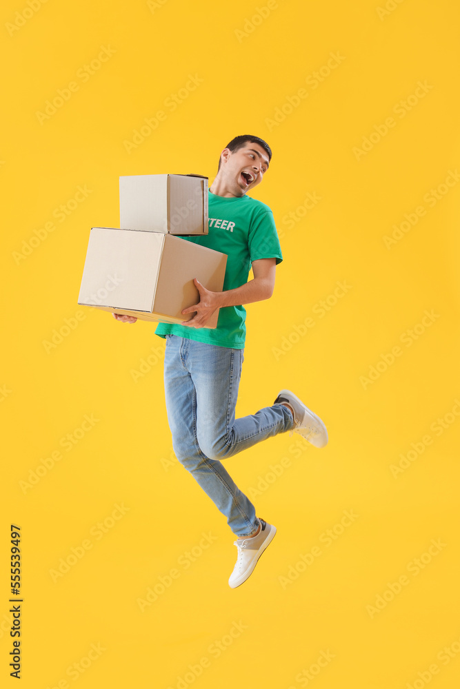 Young volunteer with cardboard boxes jumping on yellow background Young volunteer with cardboard boxes jumping on yellow background
