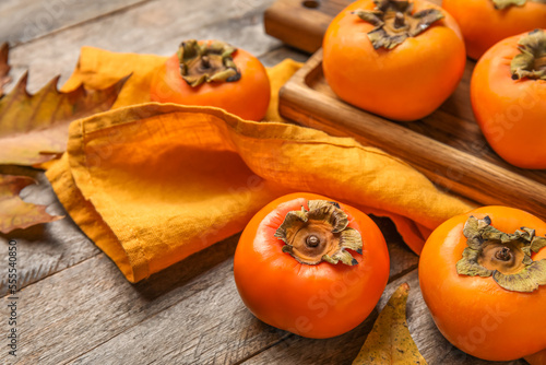 Fotografia Wooden board with ripe persimmons on wooden background, closeup