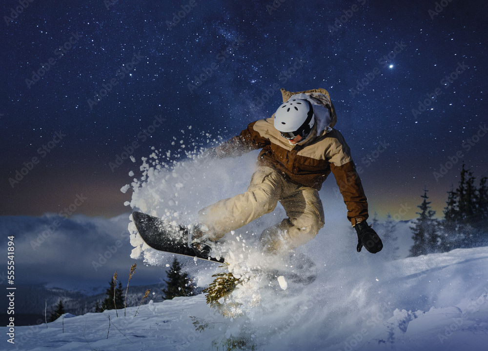 freestyle snowboarder is jumping with snowboard under the starry night sky