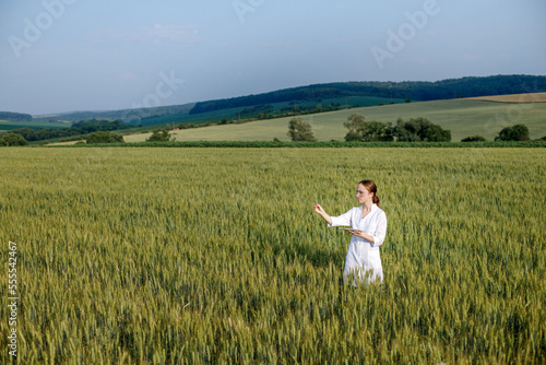 Scientist technologist in a white coat on a young wheat field writes down data on this year's crop on a smart tablet © volody10