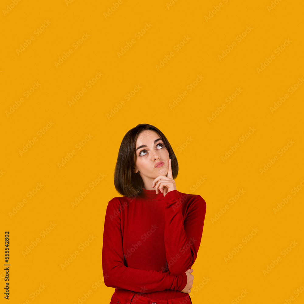 Curious pensive young woman looking at copy space on orange Curious pensive young woman looking at copy space on orange