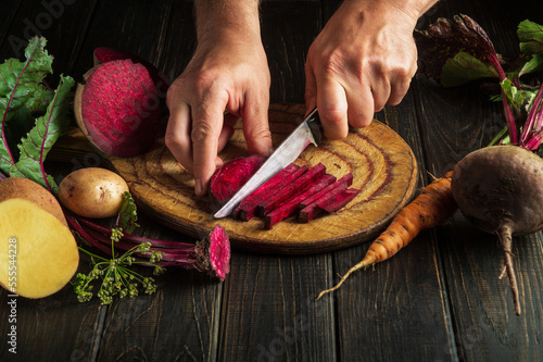Chef cuts red beets into small pieces on a kitchen cutting board before preparing a vegetarian meal. Copy space