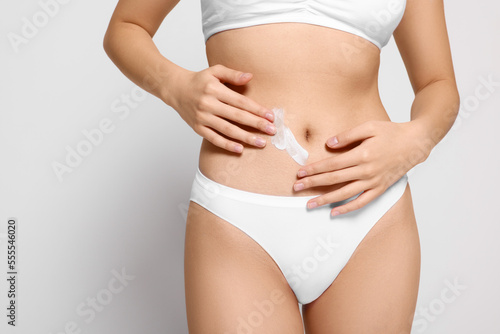 Woman with body cream smear on belly against light grey background, closeup. Space for text © New Africa