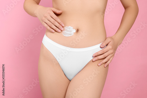 Woman applying body cream on belly against pink background, closeup © New Africa