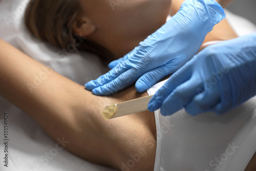 Young woman undergoing hair removal procedure of armpits with sugaring paste in salon, closeup