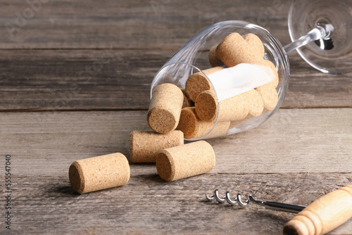 Glass with wine corks and corkscrew on wooden table