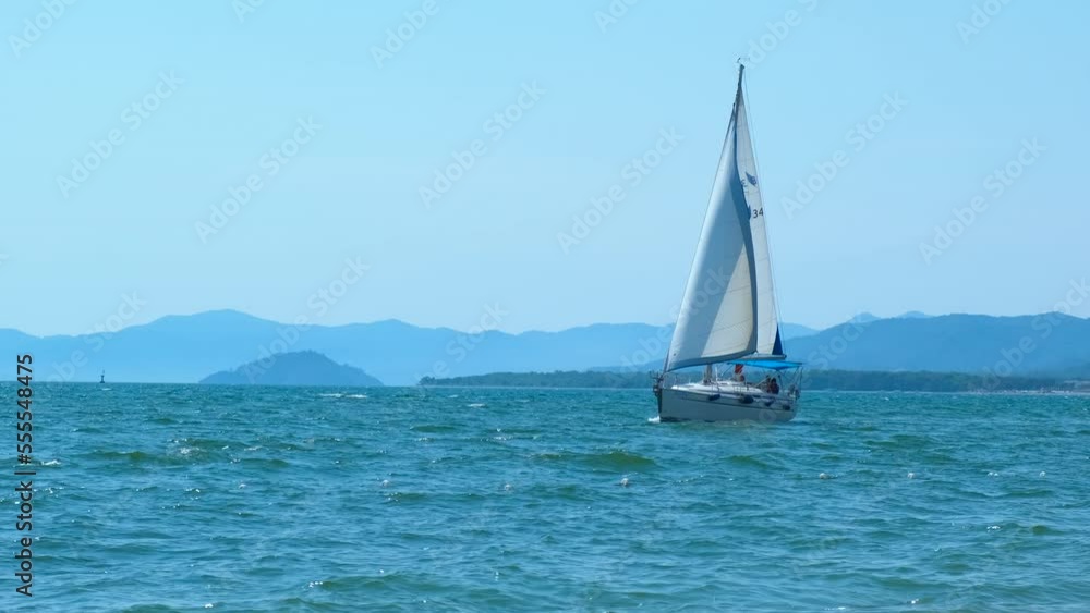 One yachting with white sails in open water. One yacht sailing with white sails in the open air against island hills. One yachting with white sails in open water. One yacht sailing with white sails in the open air against island hills.