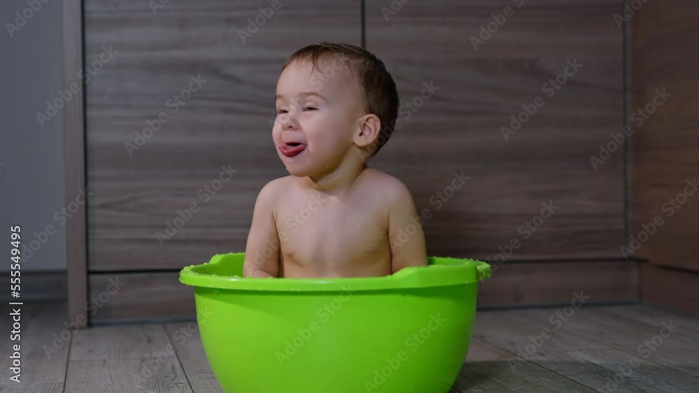 Adorable Caucasian baby boy sitting in the washbowl. Lovely kid shows the tongue and splashes water on the floor happily. Adorable Caucasian baby boy sitting in the washbowl. Lovely kid shows the tongue and splashes water on the floor happily.