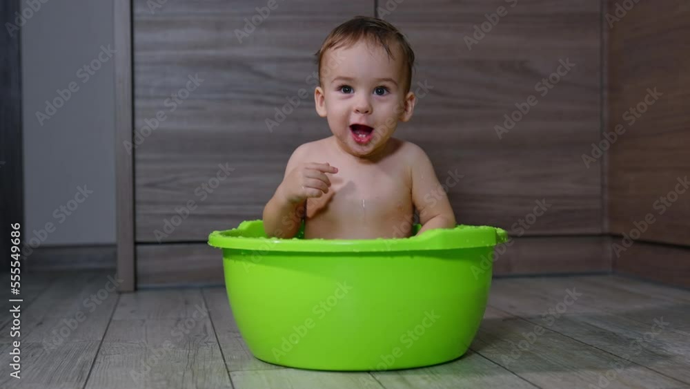 Washing time for a cute little toddler. Kid sits in a washbowl opening mouth, making noise and looking around. Washing time for a cute little toddler. Kid sits in a washbowl opening mouth, making noise and looking around.