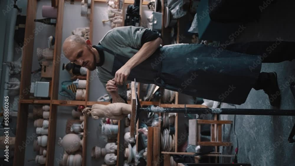 Full-length portrait of a young bearded sculptor molding by hands a limestone figurine in workshop. Full-length portrait of a young bearded sculptor molding by hands a limestone figurine in workshop.