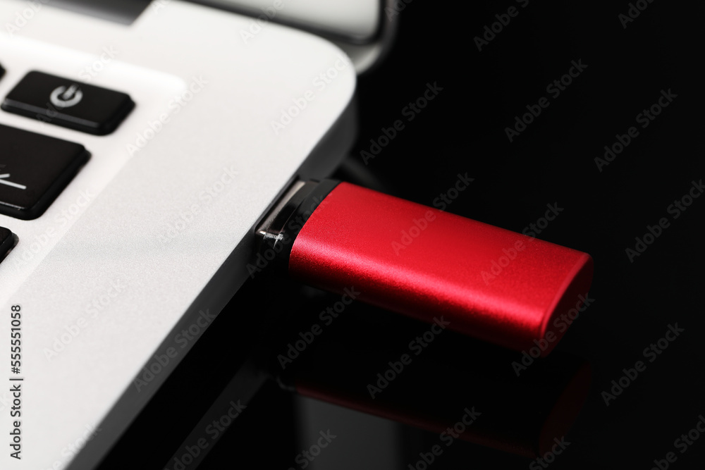 Modern usb flash drive attached into laptop on black table, closeup Modern usb flash drive attached into laptop on black table, closeup
