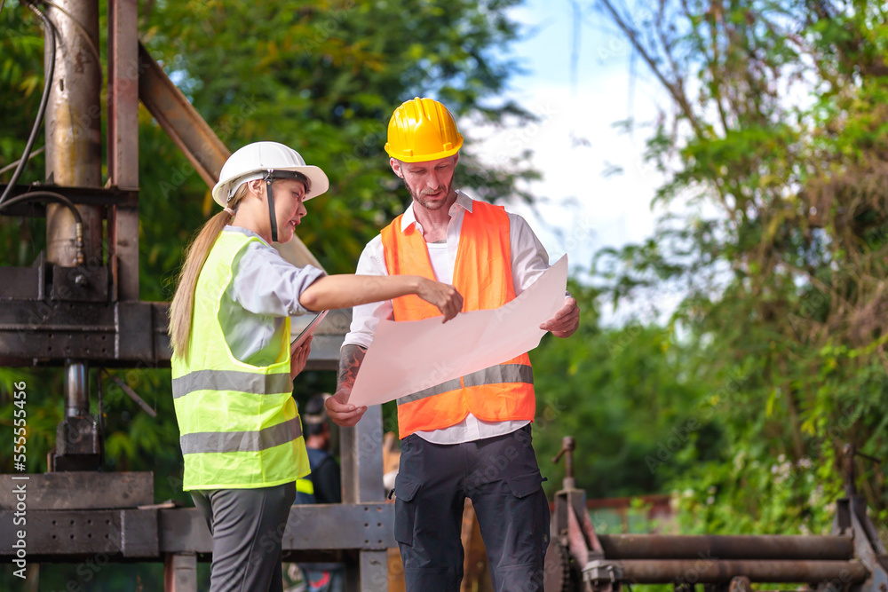 Male and female industrial engineers in Hard Hats discussing new projects while using laptops. They make gestures as they work in a heavy industrial factory. Male and female industrial engineers in Hard Hats discussing new projects while using laptops. They make gestures as they work in a heavy industrial factory.
