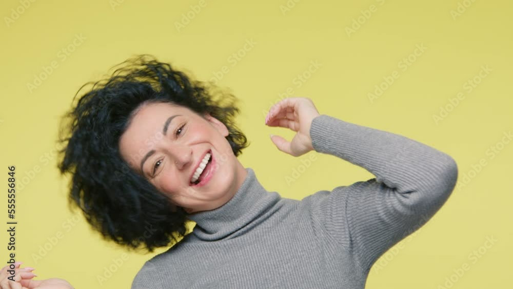 Close up portrait gorgeous mature smiling woman 40s dancing joyfully, short dark curly hair develops from side to side, slow motion on yellow background. Positive Emotions, freedom concept slow motion Close up portrait gorgeous mature smiling woman 40s dancing joyfully, short dark curly hair develops from side to side, slow motion on yellow background. Positive Emotions, freedom concept slow motion