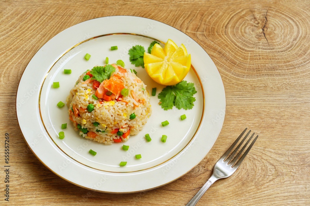 Fried rice with smoked salmon,eggs,carrots,garlics,onions,green peas,spring,soy sauce and peppers onions  on plate with wooden table background.Top view.Copy space