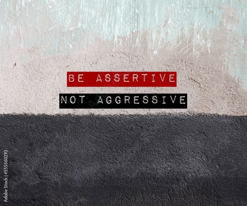 Two tone grunge wall with text written BE ASSERTIVE NOT AGGRESSIVE - concept of standing up for oneself but not violate another. Be direct, honest, express opinion without humiliate or put down anyone