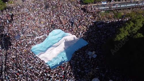 Crowd of fans waving big flag Argentine in crowded square, Buenos Aires city in Argentina. Aerial drone top-down orbiting photo