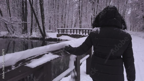 Warm dressed carefree female removing snowfall from wooden river railing in Polish winter woodland photo