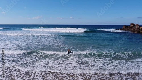 A girl entering in the water to start to surf on a beach in the Algarve, Portugal.