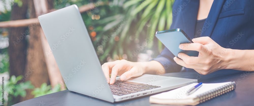 Woman working with a laptop computer and uses a cell phone in the office.