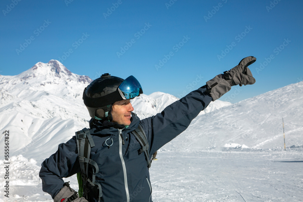 Head shot of joyful man skier shows the upward direction and wearing ski helmet and goggles