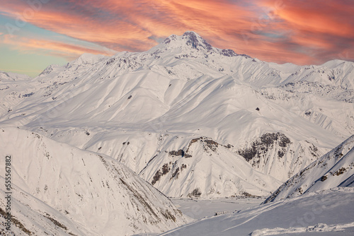 The top of Mount Kazbek under the evening orange sky with the Caucasus Mountains covered with snow