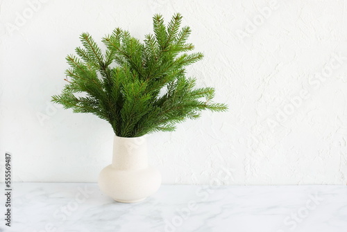 Fir tree branches in a vase near white wall on gray marble background. Copy space.Winter, new year interior composition,