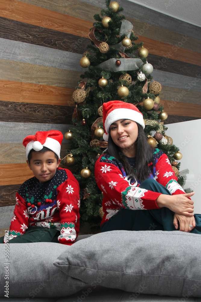 Single divorced mom and son Latino dressed in ugly sweters play in bed next to the Christmas tree with Santa hats give each other hugs and kisses show their love in solitude Single divorced mom and son Latino dressed in ugly sweters play in bed next to the Christmas tree with Santa hats give each other hugs and kisses show their love in solitude