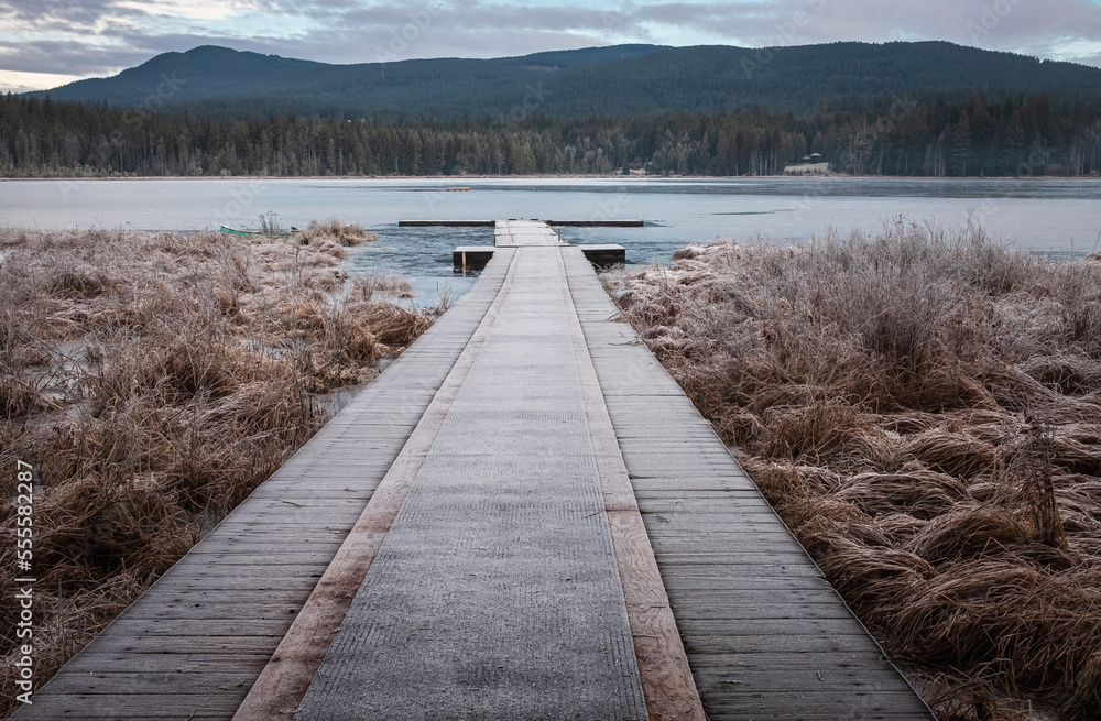 Obraz premium Wooden pier on lake site facing a beautiful mountain on a misty winter morning. Cold winters morning on a forest lake