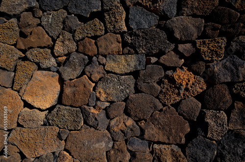 Closeup view of local wall made of volcanic rocks from past volcano eruption on Lanzarote island. Beautiful black and red brownish rough texture lava stones. Jardin de Cactus, Canary Islands, Spain.