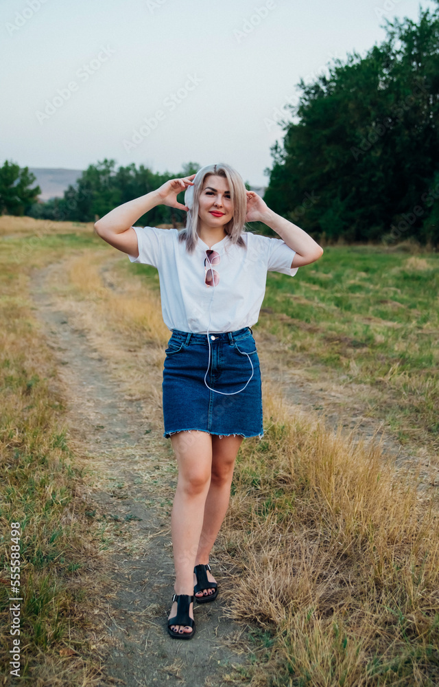 A sweet, young, happy, cheerful, pretty woman, walking outdoors in the park on a beautiful summer day. The girl listens to music with headphones. A sweet, young, happy, cheerful, pretty woman, walking outdoors in the park on a beautiful summer day. The girl listens to music with headphones.