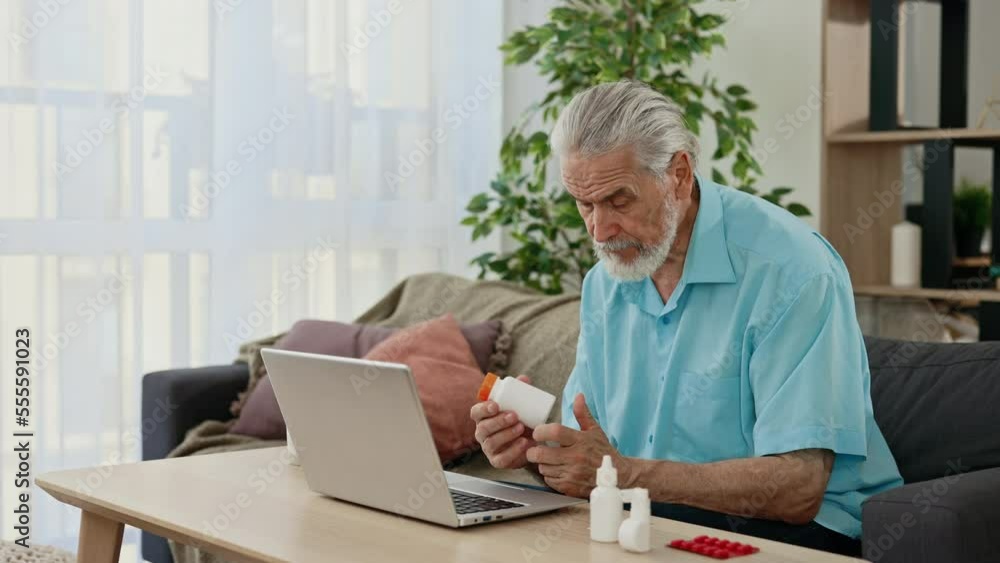 Senior male patient sit in living room using laptop to video call with doctor showing medicine on Telemedicine platform during lockdown.Technology and health care concept Senior male patient sit in living room using laptop to video call with doctor showing medicine on Telemedicine platform during lockdown.Technology and health care concept